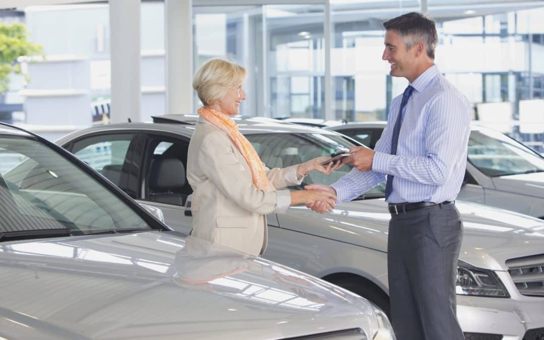 A man handing a woman keys at a car dealership