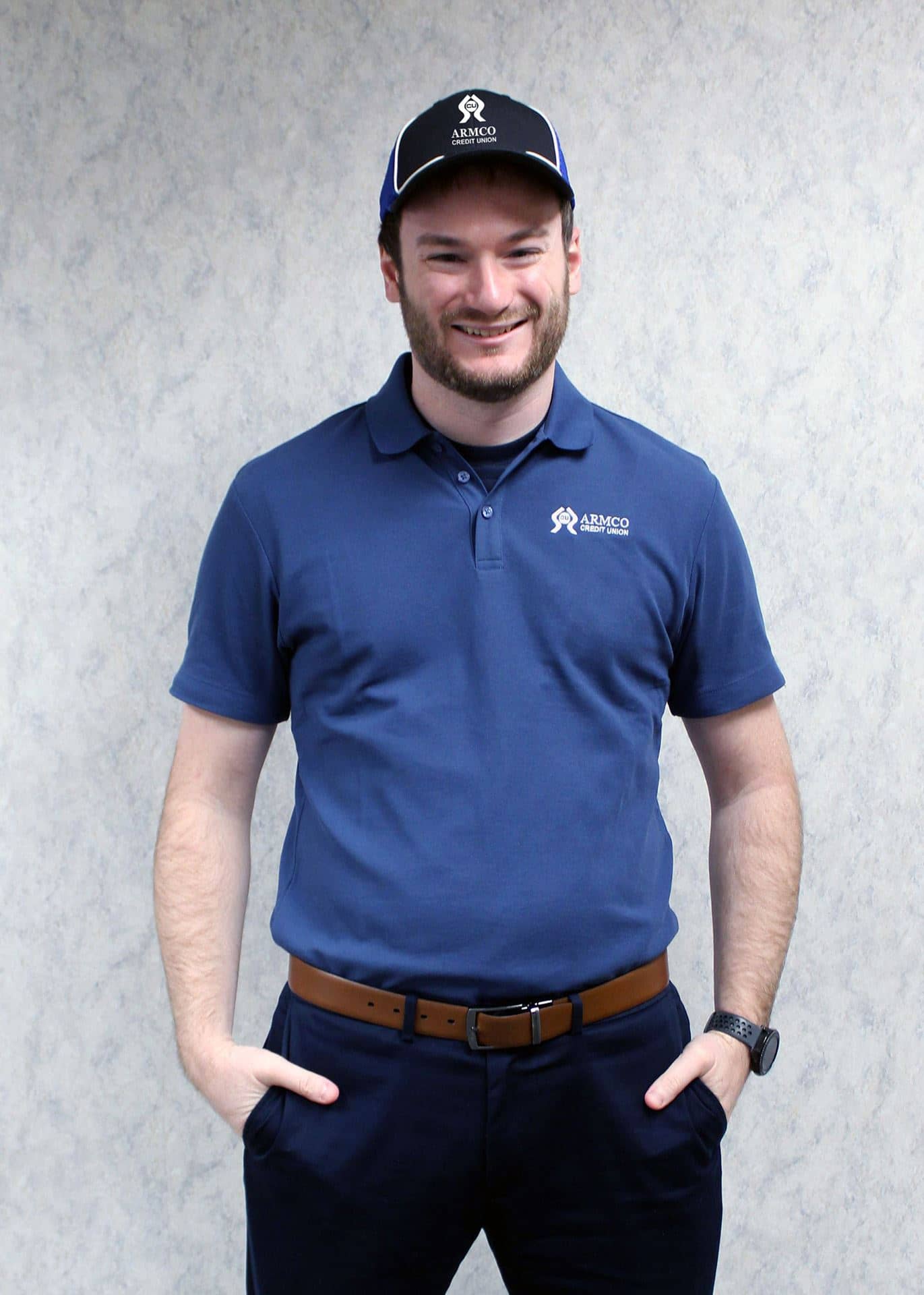 A man wearing the navy Armco CU polo shirt and baseball hat.